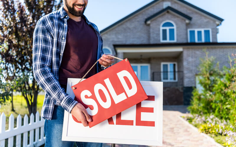 man selling his house holding a sign that says sold